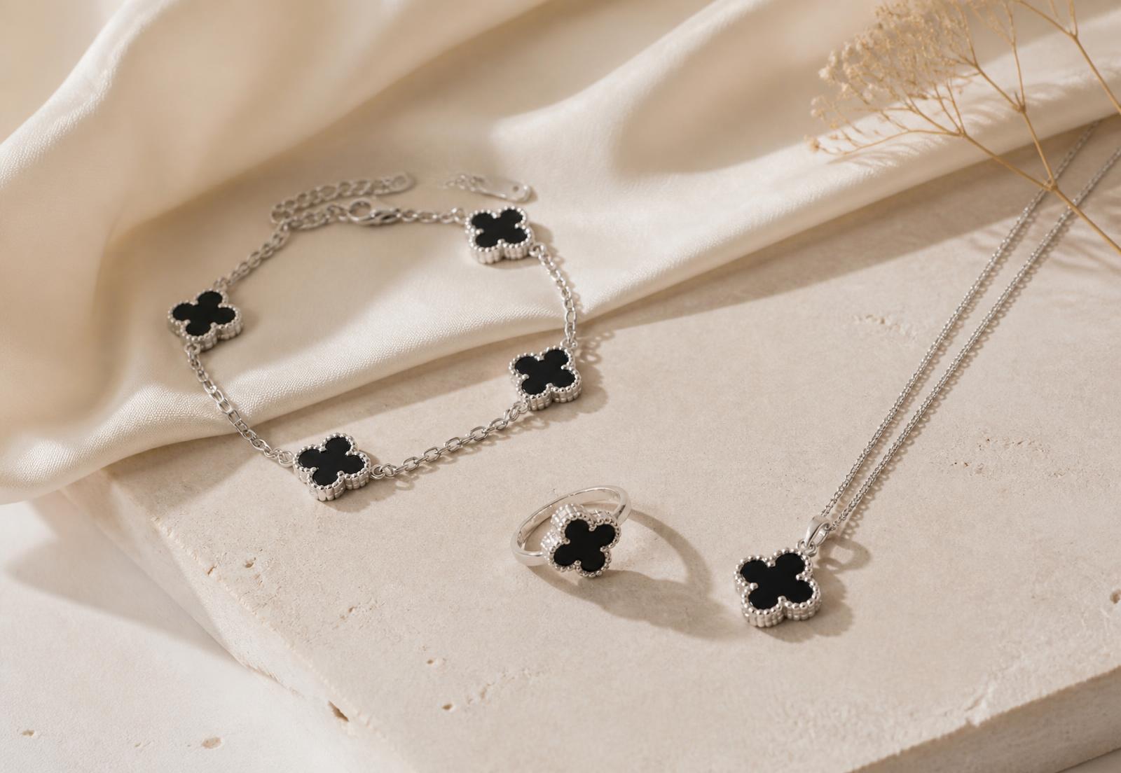 Silver clover bracelet, pendant necklace and ring with black onyx on a neutral stone surface