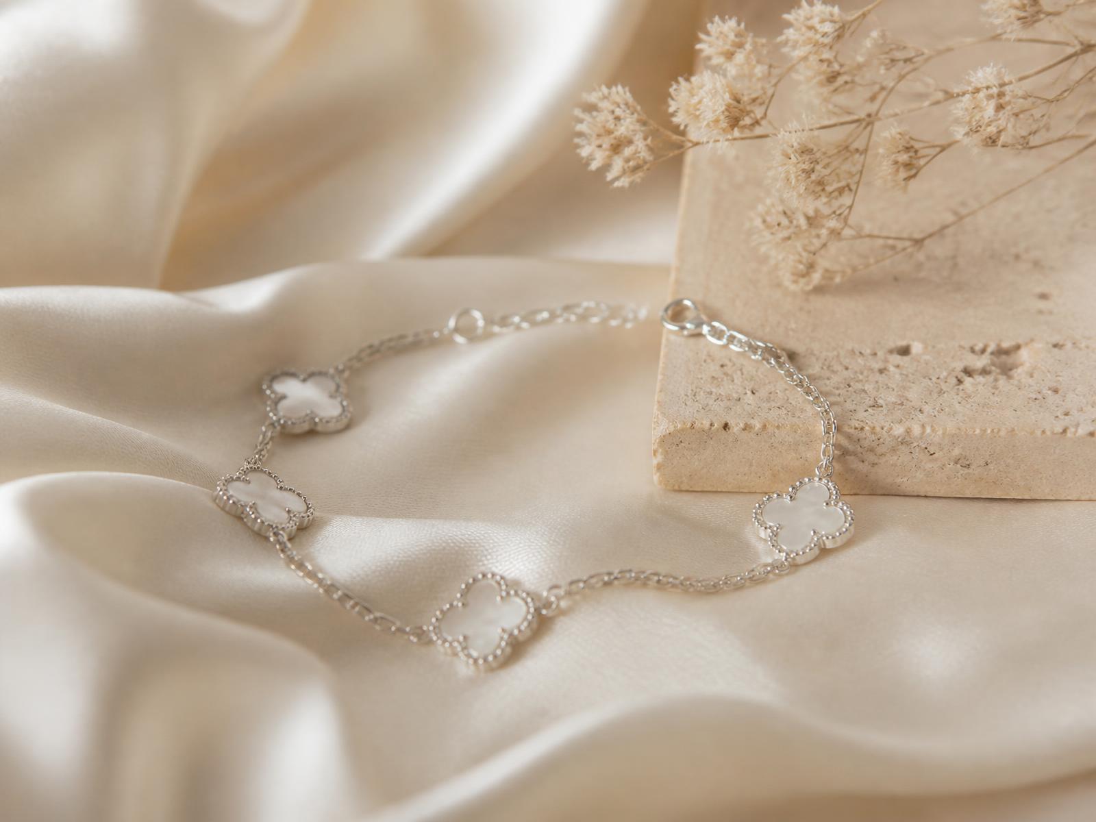 Sterling silver clover bracelet resting on cream silk beside a stone plinth